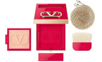 An elegant red and gold compact featuring a blush powder with a "V" logo, accompanied by a soft brush and a gold chain.